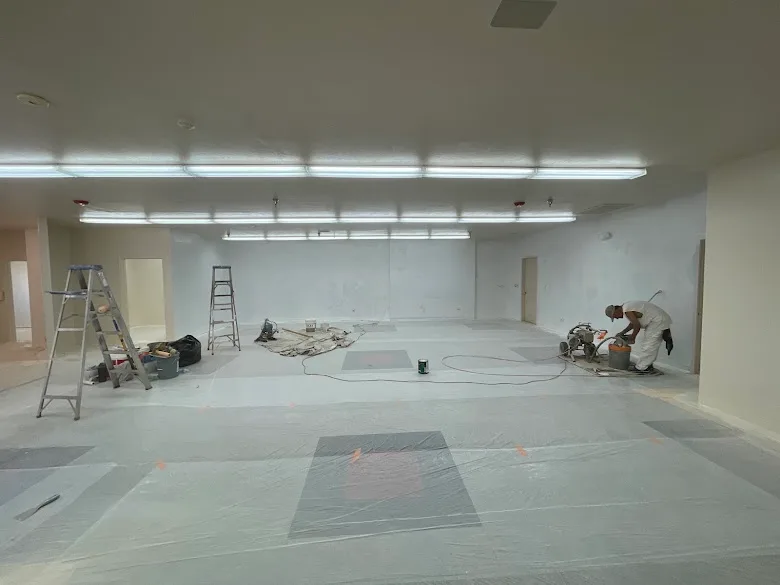 JLM Painting painter spraying a large commercial interior with floors fully covered in plastic